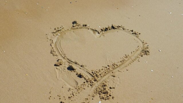 A romantic heart shape drawn on a sandy beach in 4k slow motion 120fps