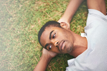 Face, relax and thinking with black man in garden of summer home for peace, wellness or mindfulness. Nature, field and grass with thoughtful young person lying on ground from above for break or rest