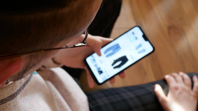 A young man choosing pants in an online store using a smartphone