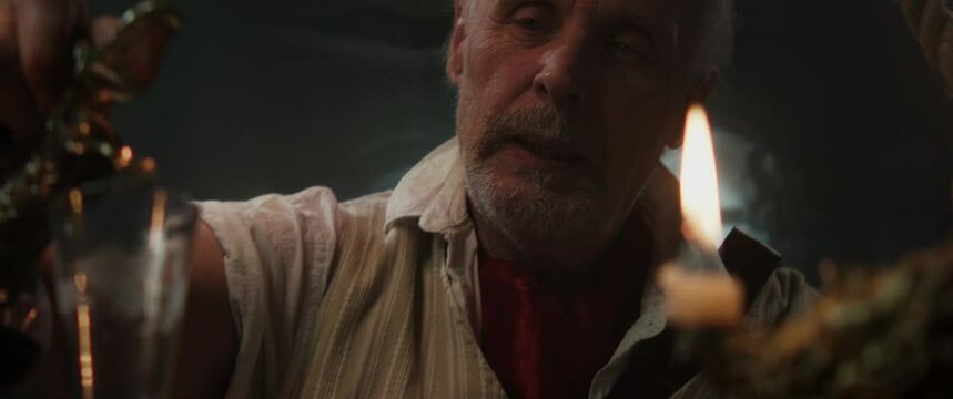 An old pirate captain eats and drinks inside vintage ship cabin