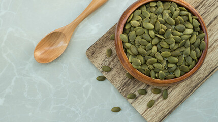 pumpkin seeds in wooden bowl on cutting board and wooden spoon on table