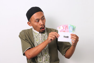 A shocked Indonesian Muslim man with a surprised expression, holds a white envelope labeled THR...