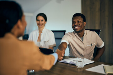 A black male doctor doing a handshake with a businesswoman from another company, having a meeting.