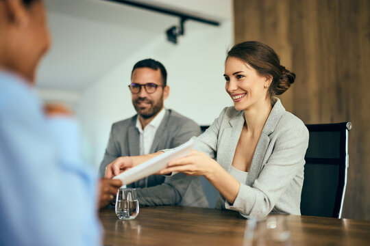 Focus on the smiling businesswoman giving a document to a client, during the meeting room.