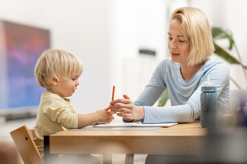 Caring young Caucasian mother and small son drawing painting in notebook at home together. Loving mom or nanny having fun learning and playing with her little 1,5 year old infant baby boy child - 748771410
