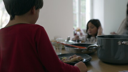 Fototapeta premium Back of little boy sitting down at lunch table with family eating food, people gathered for mealtime candid and authentic. Child observing family members from his seat