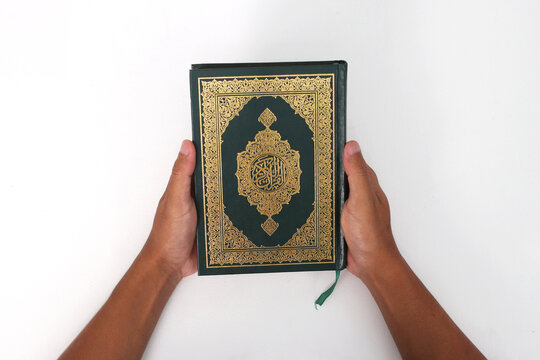 An Indonesian Muslim man holding the holy book of the Quran on a white background