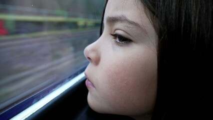 Introspective child staring at view pass by from train window during daily commute. sad 8 year old...
