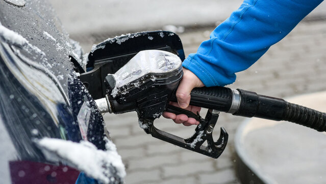 a guy in a blue hoodie holds a fuel gun - refueling a frozen car in winter and a blurred background