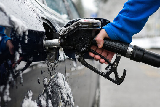 a guy in a blue hoodie holds a fuel gun - refueling a frozen car in winter and a blurred background