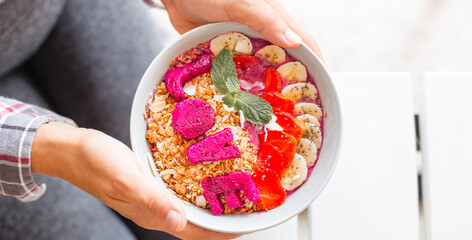 Banner female hands holding smoothie bowl with fruit and nut granola top view. Concept of healthy...
