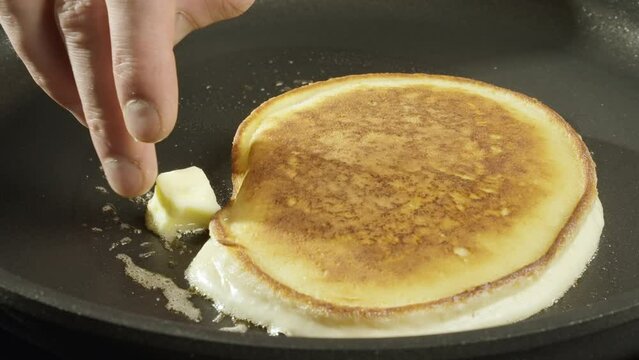 Baking pancakes at home. An American pancake is baked in a black pan. Work in the kitchen. 4k Slow motion video, 100fps. High quality footage.