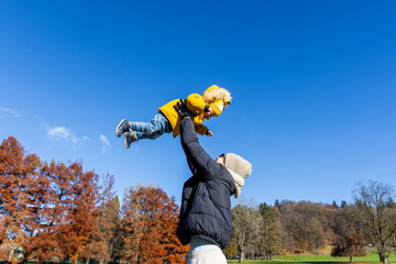 More, more,...mum, that's fun. Happy young mother throws her cute little baby boy up in the air. Mother's Day, Mather and her son baby boy playing and hugging outdoors in nature in fall - 748788073