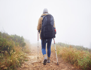 Person, hiking and back in nature with trekking sticks, winter and support for fog trail in mountain. Athlete, backpack and sport gear for safety in wet environment, slippery and walking for fitness