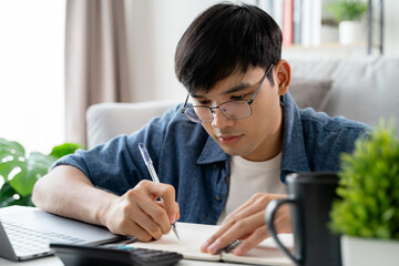  the man in casual clothes working with a laptop, computer, smart phone, calculator sitting on the sofa in the living room at home, working from home concept.