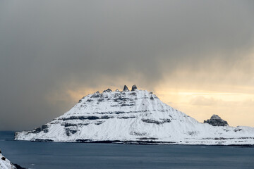 Island or rock of Tindholmur from Gasadalur in winter with snow and beautiful winter sun light. Vagar, Faroe Islands.