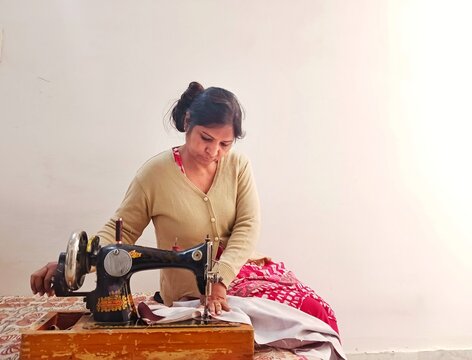 Indian housewife stitching clothes on a sewing machine at home. Independent lady concept. Sustainable clothing concept.