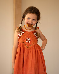 Little beautiful caucasian girl in orange dress eating tasty pancakes. 