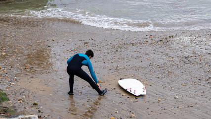 Surfer adjusting wetsuit on pebble beach with surfboard, copy space.