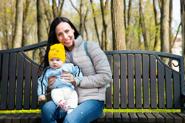Fototapeta premium A beautiful, young attractive mother, with a little boy, son, are sitting on a bench in a spring park.