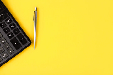 A flat lay or top view of a gray pen with a calculator on a bright yellow background with blank...