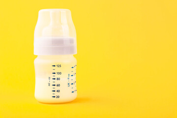 White plastic baby bottle with pacifier, rich in baby food, on yellow background. Copy space.