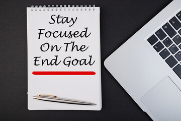 STAY FOCUSED ON THE END GOAL notepad writing concept on dark background with pen.