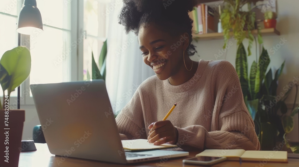 Aufkleber an african american woman in a happy mood working on her laptop while taking notes in a notebook, a 