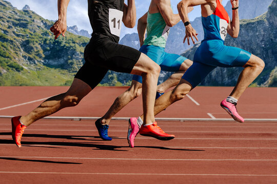group male athletes running on red track stadium on background mountains and sky. muscles taut, competing fiercely