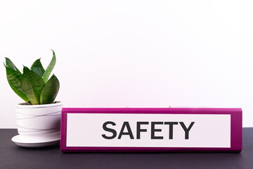 Folder with the text label Safety lies on a dark table with a flower and a light background.