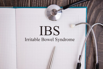 Notebook page with IBS Irritable Bowel Syndrome text, on a table with a stethoscope and pen,...