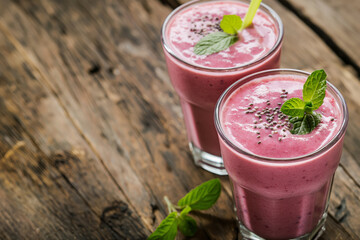 Berry smoothies in glasses, garnished with mint and chia seeds, on a rustic wooden table.