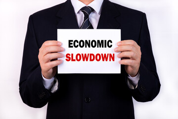 A businessman is holding a tablet with the text Economic Slowdown in front of him in his hands. Business concept