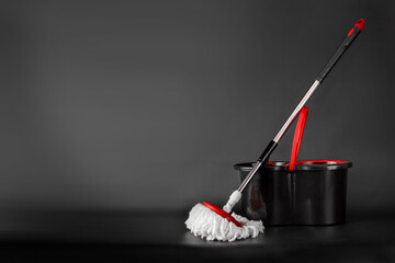 Cleaning concept mop and bucket. Cleaning products and spin mop with red details on the floor in the grey-black background