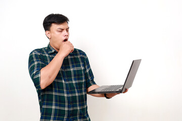 Sleepy young asian college student yawning while holding a laptop