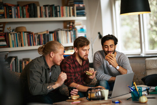 Three men studying with laptop in a home with books and snacks