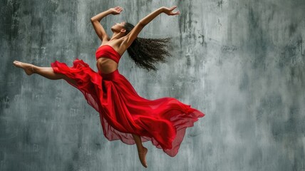 exuberant female dancer mid-air in a vibrant red dress against a textured grey backdrop, embodying...
