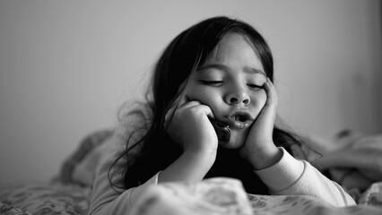 Sad depressed little girl laid in bed holding head with hands in chin, close-up face of melancholic...