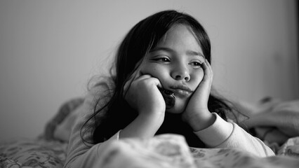 Sad depressed little girl laid in bed holding head with hands in chin, close-up face of melancholic...
