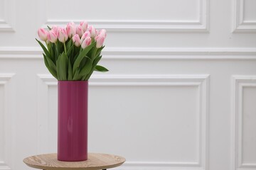 Beautiful bouquet of fresh pink tulips on table near white wall. Space for text