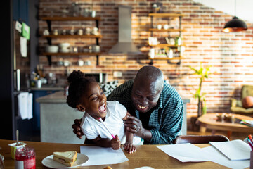 Grandfather laughing with granddaughter while doing homework in kitchen - obrazy, fototapety, plakaty