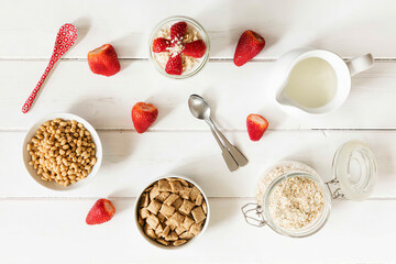 Bowls of whole meal oat cushions and oatmeal flakes, glass of porridge, strawberries and a milk jug