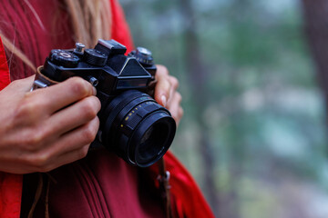 Fototapeta premium A girl takes pictures with a film camera in a fashionable hipster style. A girl travels happily with a vintage camera.