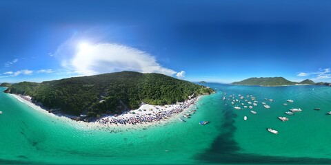 360 aerial photo taken with drone of crowded beach with crystal green waters, boats docked, and...