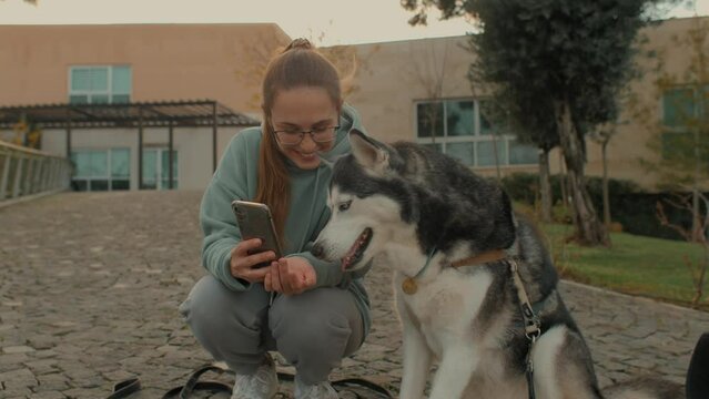 Smiling young woman and Husky dog posing making selfie photo video together use smartphone outdoor