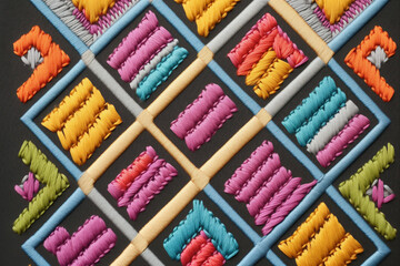 A close-up of colorful decorative embroidery on a gray background. Rhombuses of yellow and blue creating an abstract geometric pattern. AI-generated