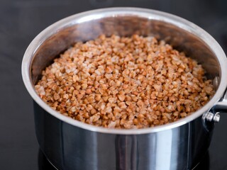 A close-up shot of buckwheat cooking in a steel pot on the black stove top.