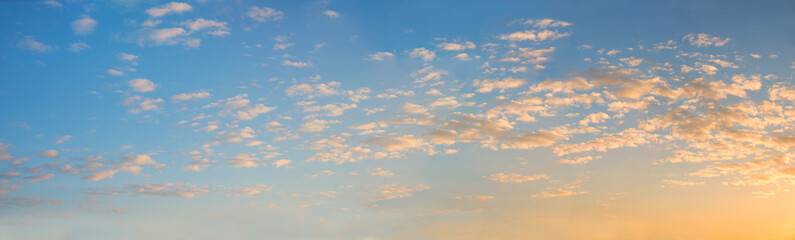 wide blue sky panorama with fleecy clouds and yellow shine, at dawn