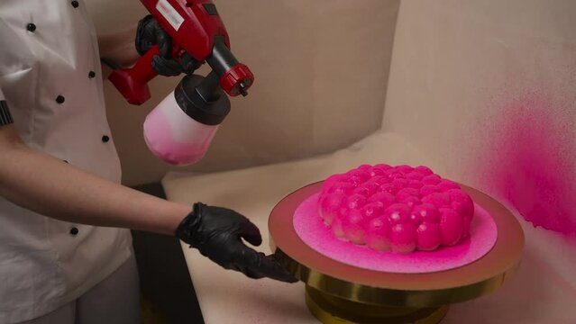 The cook applies pink paint to the cake.