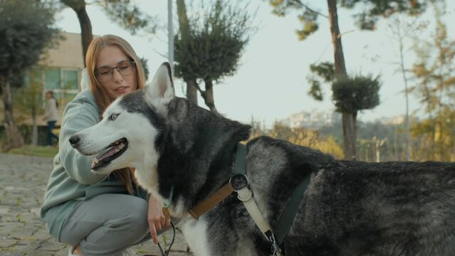 Caring young woman stroking hugging Husky dog with love and tenderness at autumn city park